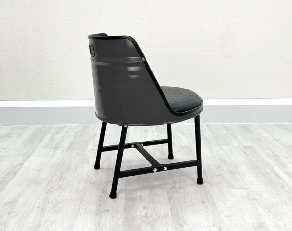 Seitliche Ansicht von Ölfass Esszimmer Stuhl in Grau mit gesprayten Backsteinen auf der Rückseite, mit schwarzem Sitzpolster und schwarzen Metallbeinen auf weißem Holzboden vor weißem Hintergrund