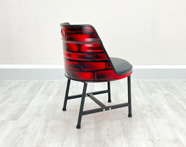 Seitliche Ansicht von Ölfass Esszimmer Stuhl in Rot mit gesprayten Backsteinen auf der Rückseite, mit schwarzem Sitzpolster und schwarzen Metallbeinen auf weißem Holzboden vor weißem Hintergrund