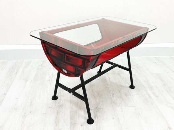 Roter Upcycling Ölfass Tisch mit Stauraum im Inneren und außen aufgesprayten Backsteinen mit Glastischplatte vor weißer Wand auf weißem Holzboden