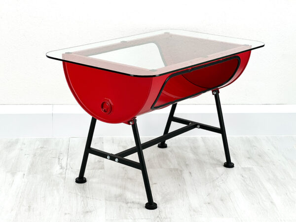 Roter Upcycling Ölfass Tisch mit Stauraum im Inneren und Glastischplatte auf schwarzen Metallfüßen vor weißer Wand auf weißem Holzboden