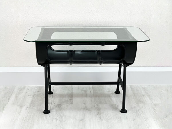 Uni schwarzer Ölfass Tisch Mick von der Seite fotografiert mit Stauraum im Inneren und Glastischplatte auf schwarzen Metallfüßen vor weißer Wand auf weißem Holzboden