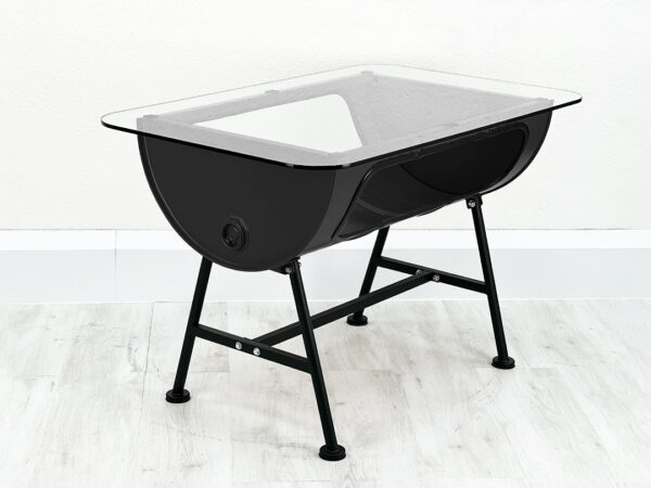 Uni schwarzer Ölfass Tisch mit Stauraum im Inneren und Glastischplatte auf schwarzen Metallfüßen vor weißer Wand auf weißem Holzboden