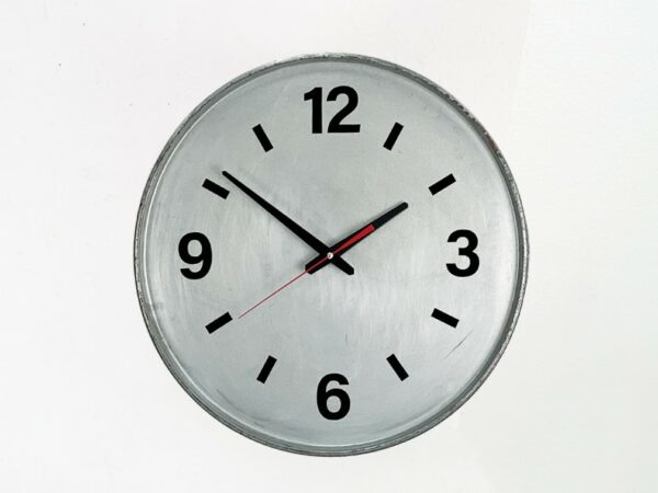 Verzinkte Ölfass Wanduhr mit schwarzem Ziffernblatt, schwarzen Zeigern und rotem Sekundenzeiger vor weißem Hintergrund