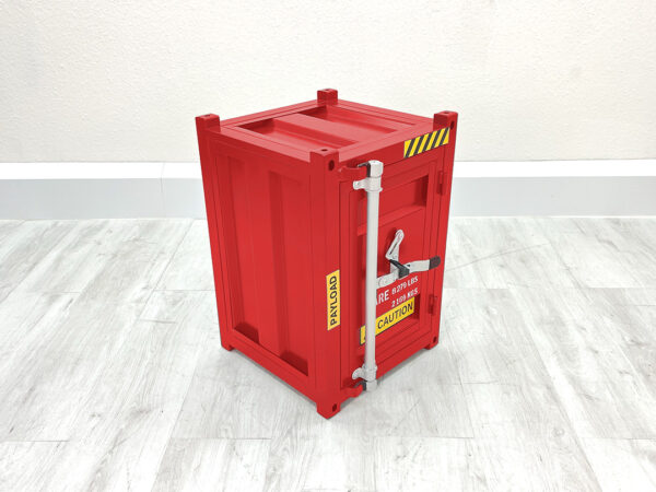 Roter kleiner Metallschrank in Übersee Container Optik mit geschlossener Tür auf weißem Holzboden vor weißer Wand